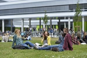 Drei Studierende sitzen auf den Grünflächen der Universität Bielefeld