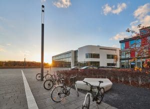 asphaltierter Vorplatz des Neuen Hörsaalzentrums auf dem Campus Poppelsdorf. Im Hintergrund ist ein Sonnenuntergang zu sehen und im Vordergrund stehen einige Fahrräder.