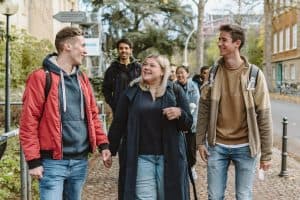 Studierende halten sich auf dem Campus Poppelsdorf auf. Drei Studierende im Vordergrund unterhalten sich lachend miteinander. Eine größere Gruppe ist im Hintergrund zu sehen.